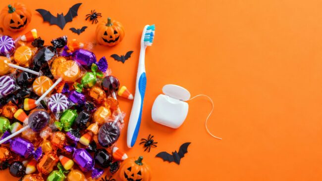 Halloween candy pile with toothbrush and dental floss on orange background – dentist and oral hygiene reminder flat lay